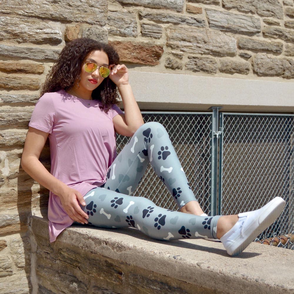 Model posing by sitting on ledge wearing puppy love pattern leggings by Jolina Boutique