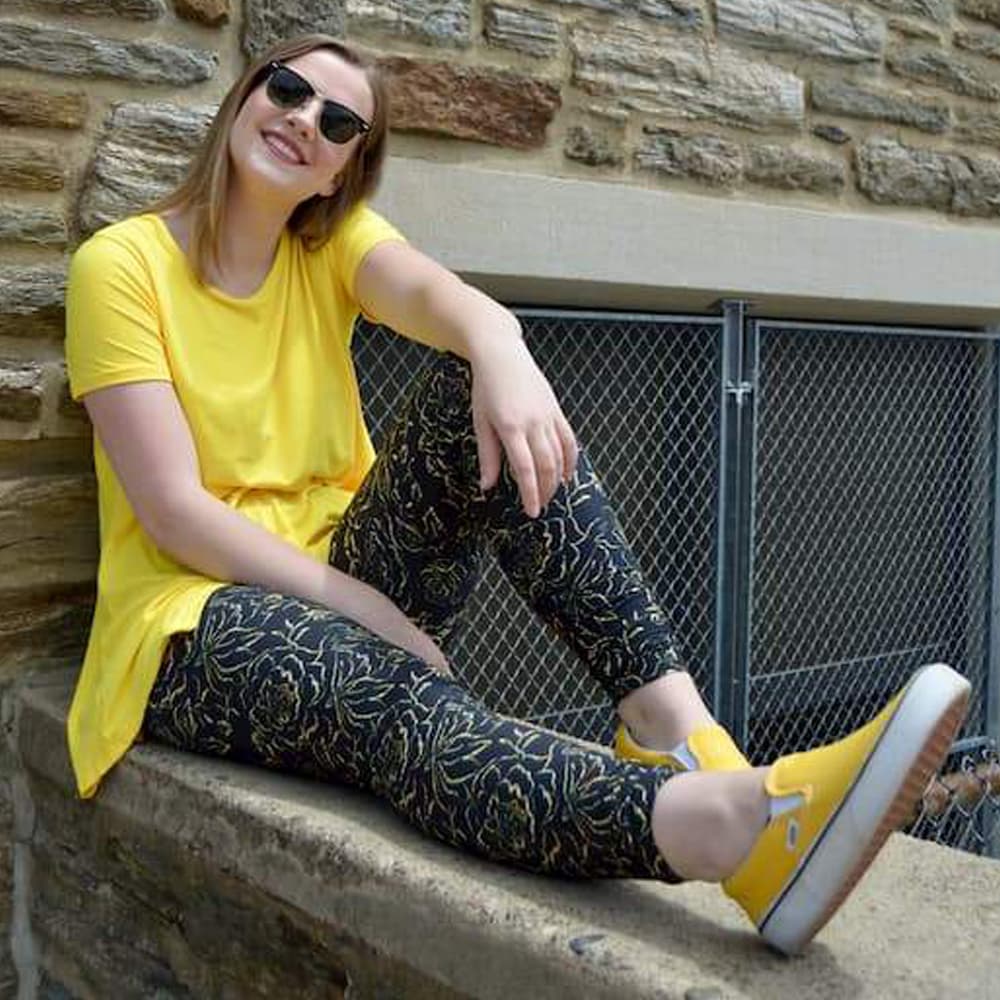 Model sitting on ledge wearing golden rose pattern leggings by Jolina Boutique