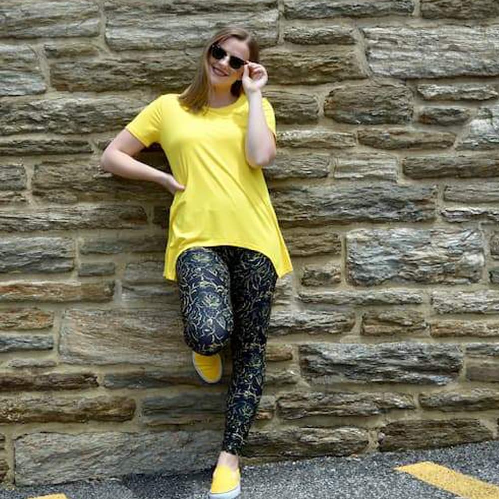 Model posing with back against the wall wearing golden rose pattern leggings by Jolina Boutique